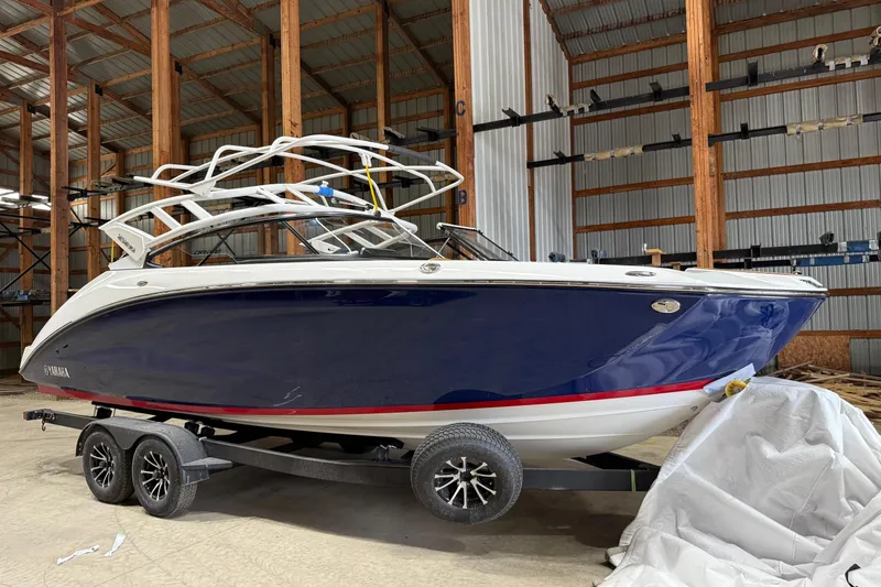 The Image of 2025 Yamaha Boats 252SD in storage, featuring sleek blue and white design on a trailer. - 0