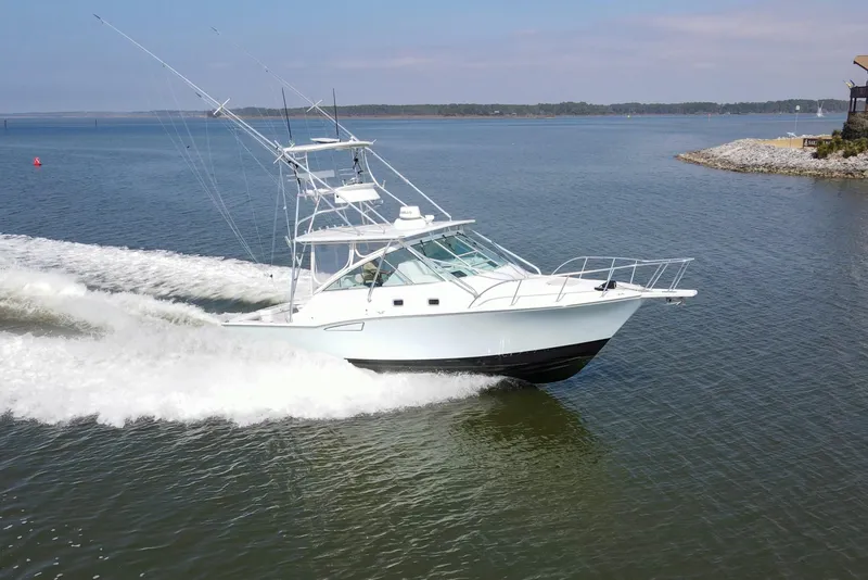 Slide: The Image of 1995 Cabo 35 Express boat cruising on a calm lake near the shoreline. - 2