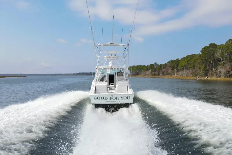 Slide: The Image of 1995 Cabo 35 Express boat cruising on a scenic waterway, leaving a wake behind. - 5