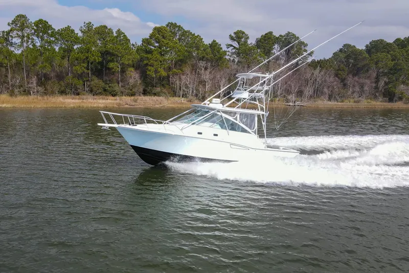 Slide: The Image of 1995 Cabo 35 Express boat cruising on a scenic waterway with lush forest backdrop. - 7