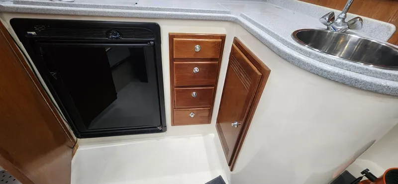 Slide: The Image of 1995 Cabo 35 Express boat kitchen with sink, fridge, and wooden cabinets. - 26