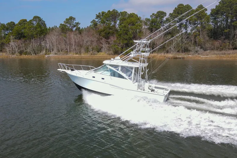 Slide: The Image of 1995 Cabo 35 Express boat cruising on a calm lake with trees in the background. - 6