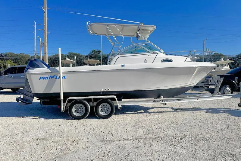 The Image of 2000 Pro-Line 22 Walkaround boat on trailer, parked outdoors under clear blue sky. - 1