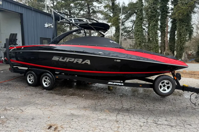 The Image of 2011 Supra Launch 242 boat with red and black design on a trailer. - 0