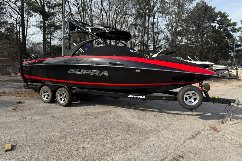 Slide: The Image of 2011 Supra Launch 242 boat on trailer, black with red accents, parked outdoors. - 2