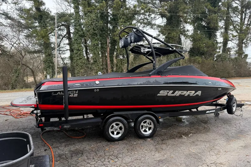 Slide: The Image of 2011 Supra Launch 242 boat on trailer, black with red accents, parked outdoors. - 4