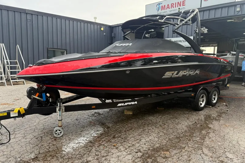 Slide: The Image of 2011 Supra Launch 242 boat in black and red, parked on a trailer outside a marine service shop. - 6