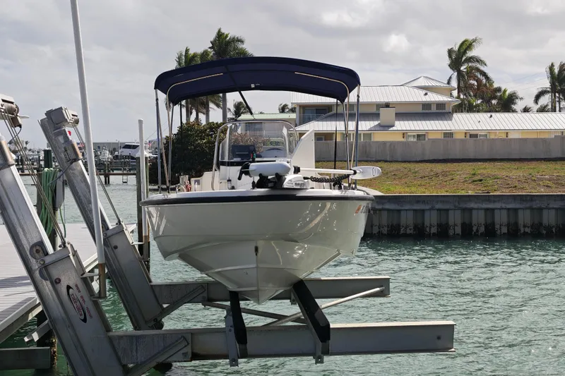 Slide: The Image of 2006 Boston Whaler 180 Dauntless boat docked on lift, with blue canopy, in marina setting. - 17