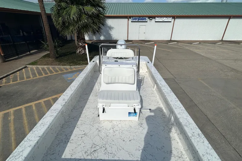 Slide: The Image of 2026 Coastal Skiff 212 boat with white interior, parked near a building. - 14