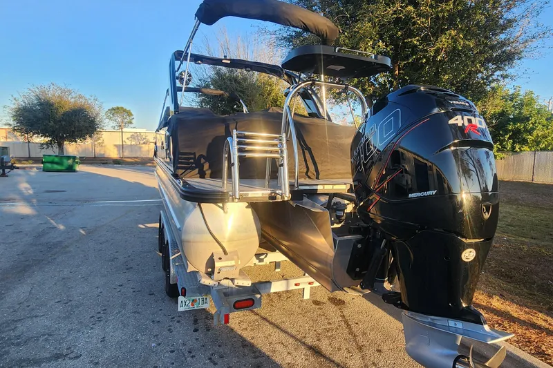 Slide: The Image of 2023 Avalon Excalibur 25' boat with Mercury 400R engine, parked outdoors. - 25