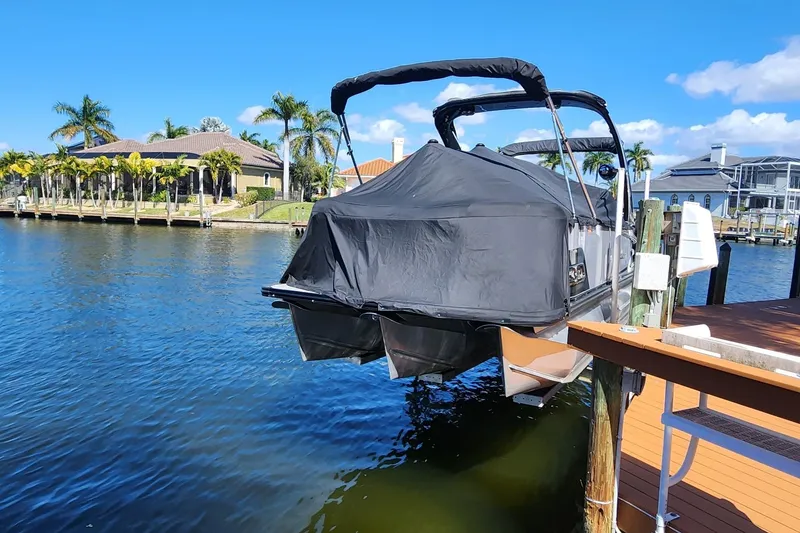 Slide: The Image of 2023 Avalon Excalibur 25' boat docked, covered, with waterfront homes and palm trees in the background. - 29
