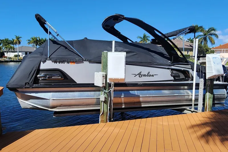 Slide: The Image of 2023 Avalon Excalibur 25' boat docked, covered, with palm trees in the background. - 30