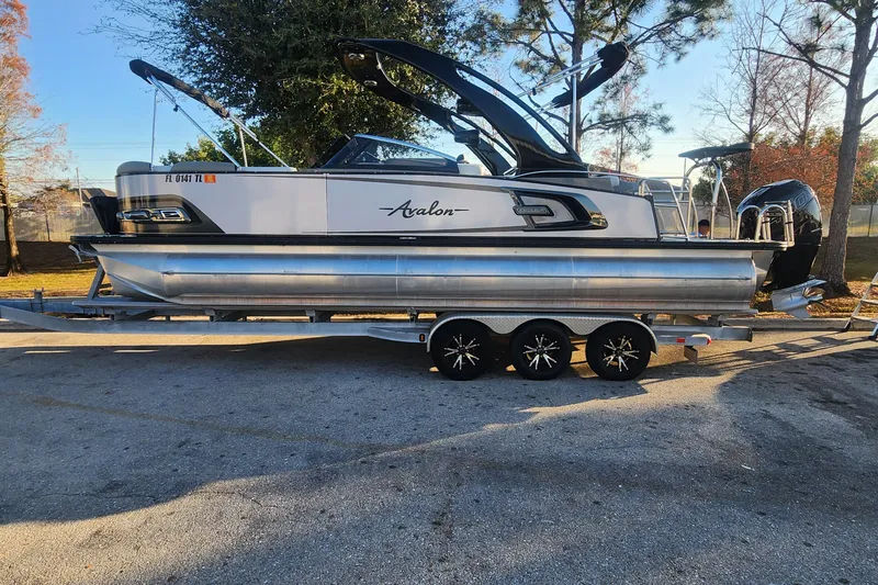 Slide: The Image of 2023 Avalon Excalibur 25' pontoon boat on trailer, parked outdoors. - 5