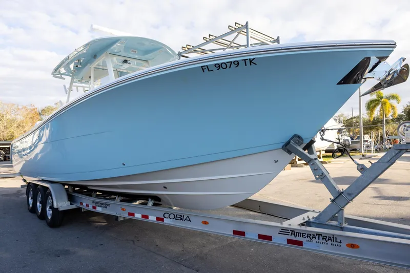 The Image of 2022 Cobia 320 Center Console boat on trailer, light blue hull, parked outdoors. - 1