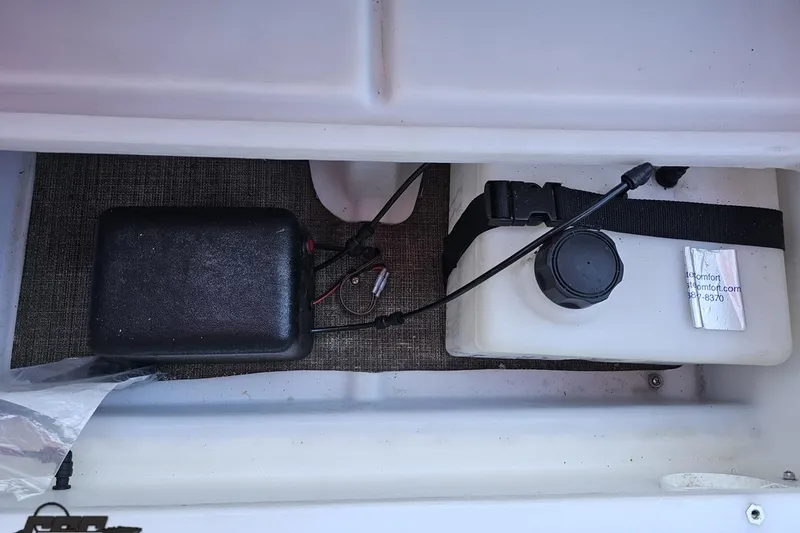 Slide: The Image of Storage compartment of a 2019 JC Tritoon Neptoon 25 Sport SL boat, featuring a battery and fluid container. - 90