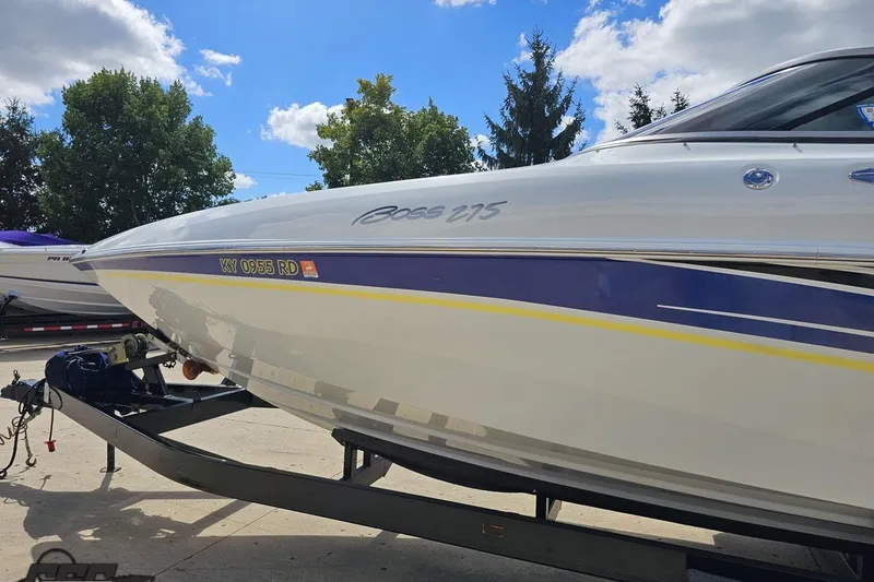 Slide: The Image of 2005 Baja 275 boat on trailer, white with blue and yellow accents, under a clear sky. - 20