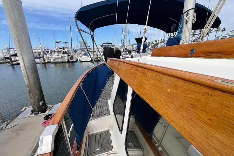 Slide: The Image of 1986 Nauticat 33' sailboat docked at marina, featuring wooden railings and blue canopy. - 15