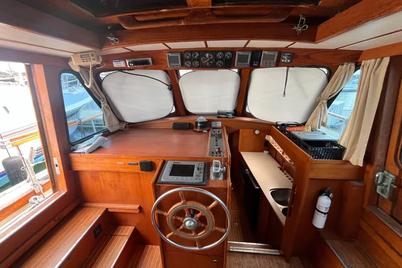 Slide: The Image of 1986 Nauticat 33' yacht interior with wooden helm, navigation instruments, and compact kitchen area. - 25