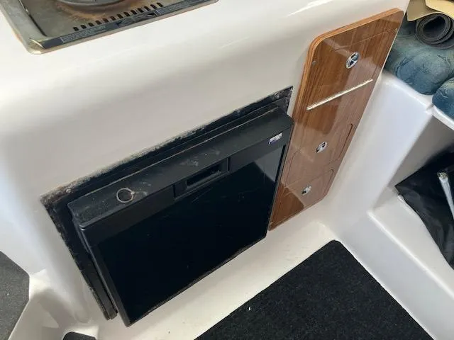 Slide: The Image of 2004 Pro-Line 30 WALK boat interior with compact fridge and wooden storage panel. - 7