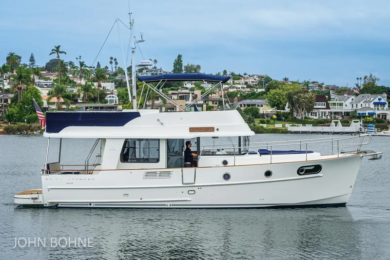 Slide: The Image of 2018 Beneteau Swift Trawler 44 cruising on a scenic waterfront with houses in the background. - 5