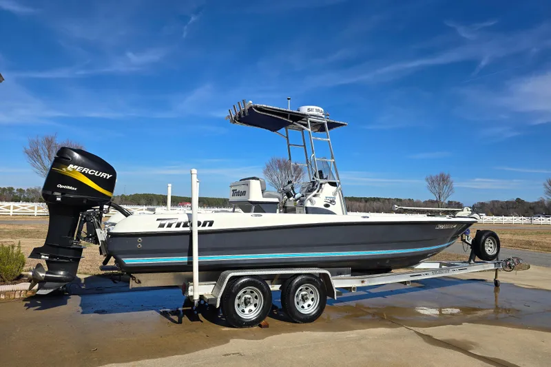 The Image of 2004 Triton 240 LTS boat on trailer with Mercury outboard motor, under clear blue sky. - 1