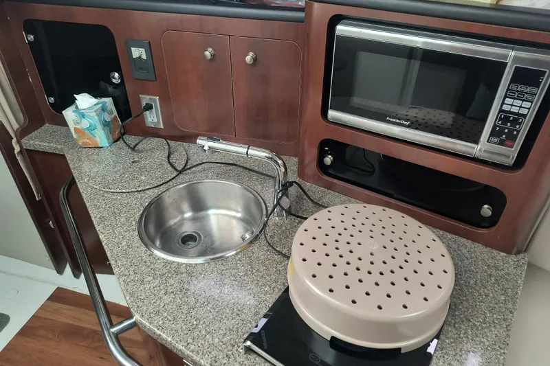 Slide: The Image of 2015 Robalo R305 Walkaround boat kitchen with sink, microwave, and countertop appliances. - 16