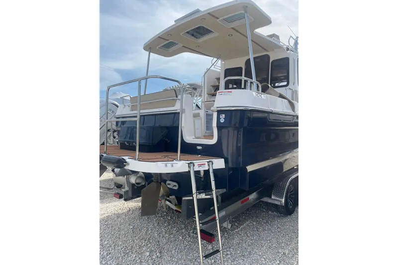 Slide: The Image of 2025 Ranger Tugs R-31 CB boat, rear view with ladder and deck, on gravel surface. - 3