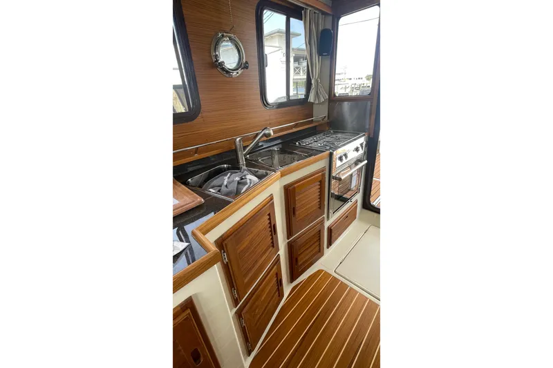 Slide: The Image of 2025 Ranger Tugs R-31 CB interior kitchen with wood cabinetry and stainless steel appliances. - 7