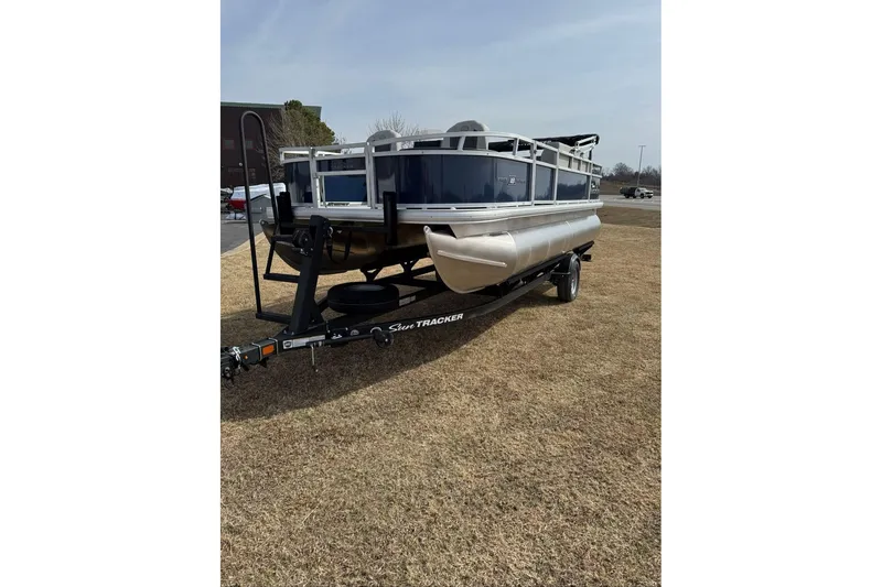 Slide: The Image of 2026 Sun Tracker Bass Buggy 18 DLX pontoon boat on trailer, parked on grass. - 13