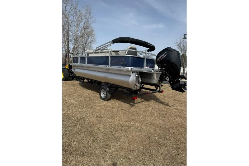 Slide: The Image of 2026 Sun Tracker Bass Buggy 18 DLX pontoon boat on trailer, parked on grass. - 14
