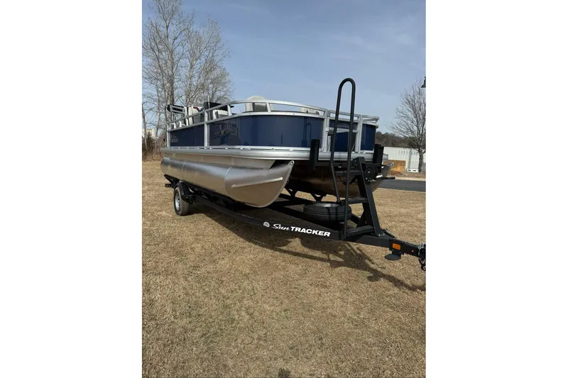Slide: The Image of 2026 Sun Tracker Bass Buggy 18 DLX pontoon boat on trailer, parked on grass. - 6
