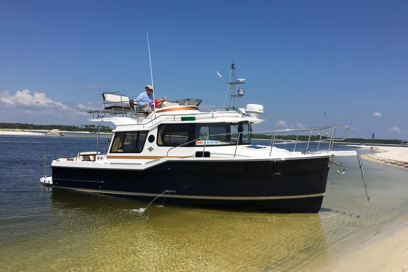 The Image of 2025 Ranger Tugs R-29 CB boat anchored on sandy shore under clear blue sky. - 0