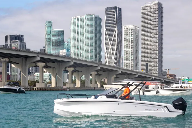 Slide: The Image of 2024 Axopar 25 Cross Top boat cruising near city skyline and bridge. - 2