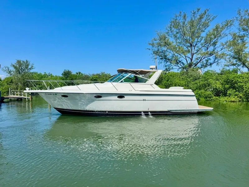 The Image of 1998 Tiara Yachts 3500 Express cruising on a serene waterway, surrounded by lush greenery. - 0
