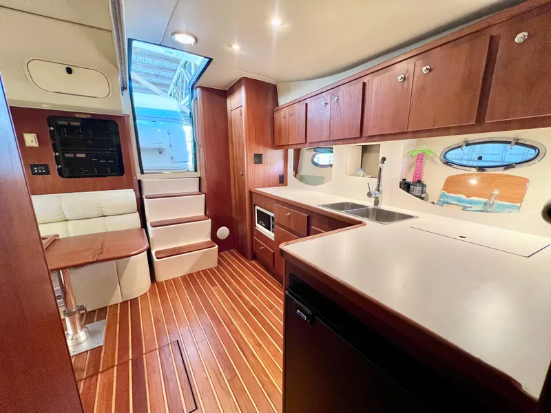 Slide: The Image of 1998 Tiara Yachts 3500 Express interior with wood cabinetry, kitchenette, and seating area. - 19
