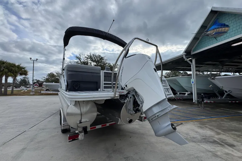 Slide: The Image of 2026 Bennington 24 MFB pontoon boat with outboard motor, parked outdoors under cloudy sky. - 14