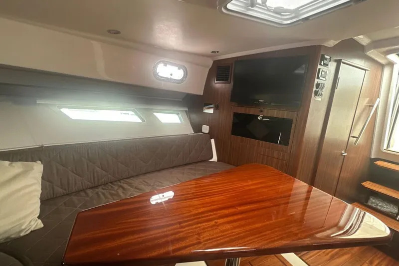 Slide: The Image of 2017 Pursuit OS 355 Offshore cabin interior with wood table, seating, and TV. - 14