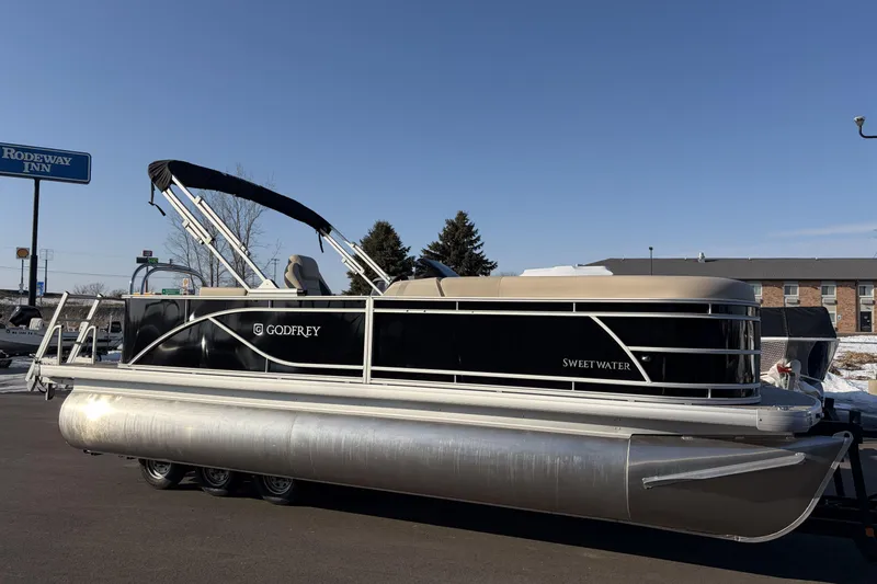 Slide: The Image of 2026 Godfrey Sweetwater 2086 C pontoon boat on trailer, parked near Rodeway Inn. - 2