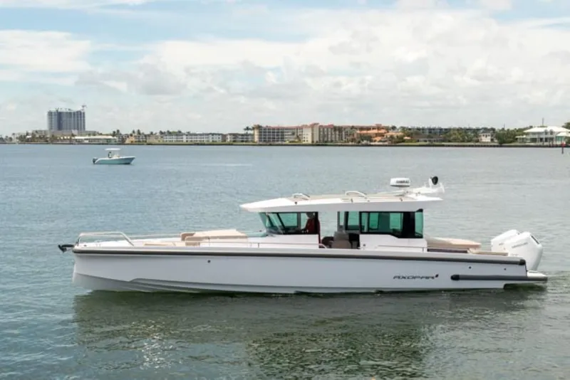 Slide: The Image of 2024 Axopar 37XC CROSS CABIN boat on calm water, cityscape in background. - 3