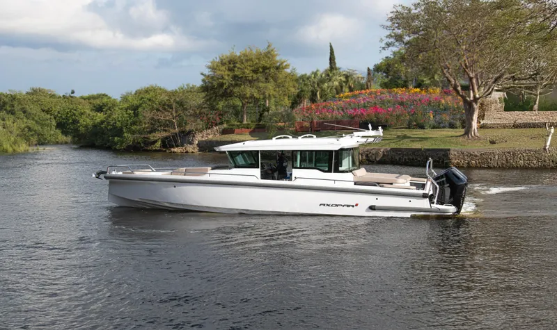Slide: The Image of 2024 Axopar 37XC CROSS CABIN boat cruising on a scenic river with lush greenery. - 2
