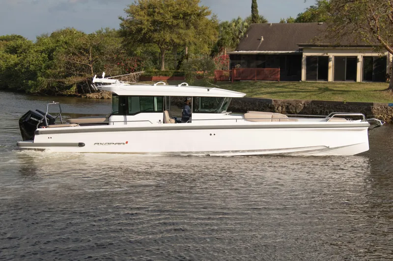 Slide: The Image of 2024 Axopar 37XC CROSS CABIN boat cruising on a calm river near a house. - 5