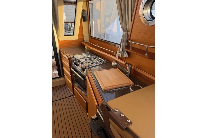 Slide: The Image of 2024 Ranger Tugs R-29 CB galley with stove, sink, and wooden cabinetry. - 10