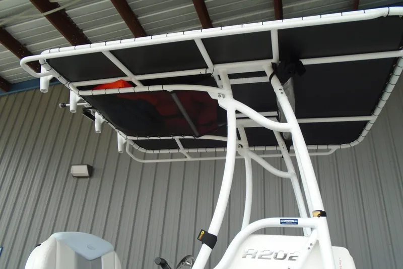 Slide: The Image of 2021 Robalo R202 Explorer boat with T-top and rod holders, under a metal roof. - 11