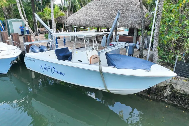 Slide: The Image of 2005 Sailfish 2660 CC boat docked near tropical foliage and a thatched-roof structure. - 2