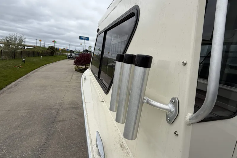 Slide: The Image of 2026 Hewescraft 240 Ocean Pro ET Hardtop with rod holders, parked on a paved path. - 13