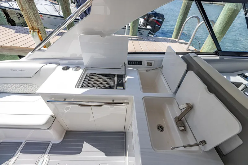 Slide: The Image of 2022 Regal LX36 boat interior with kitchenette and sink, docked by the water. - 37