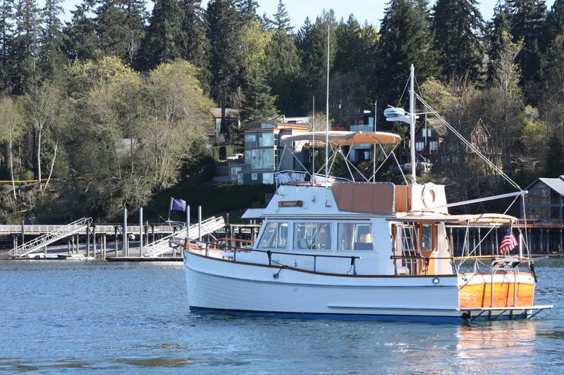 Slide: The Image of 1983 Grand Banks 32 Sedan boat on calm water near a wooded shoreline. - 3