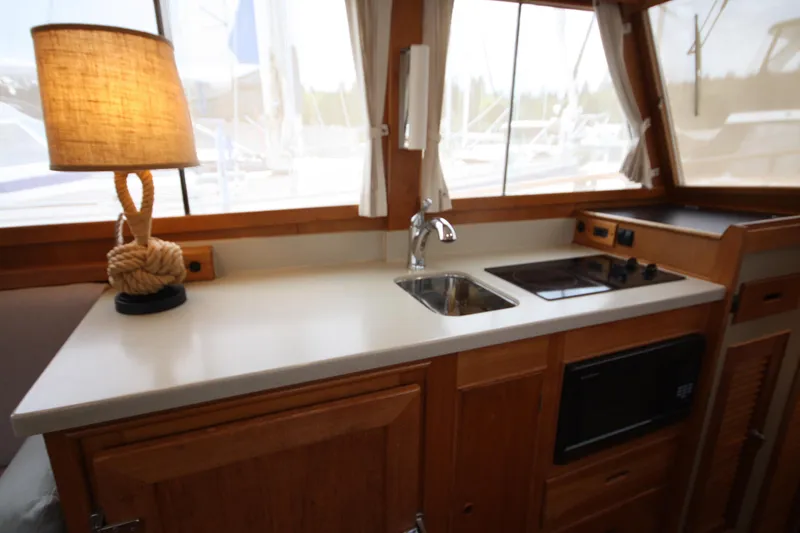 Slide: The Image of 1983 Grand Banks 32 Sedan interior with kitchenette, featuring sink, stove, and nautical lamp. - 34