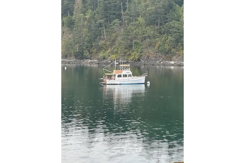 Slide: The Image of 1983 Grand Banks 32 Sedan boat anchored on a serene lake with forested backdrop. - 69