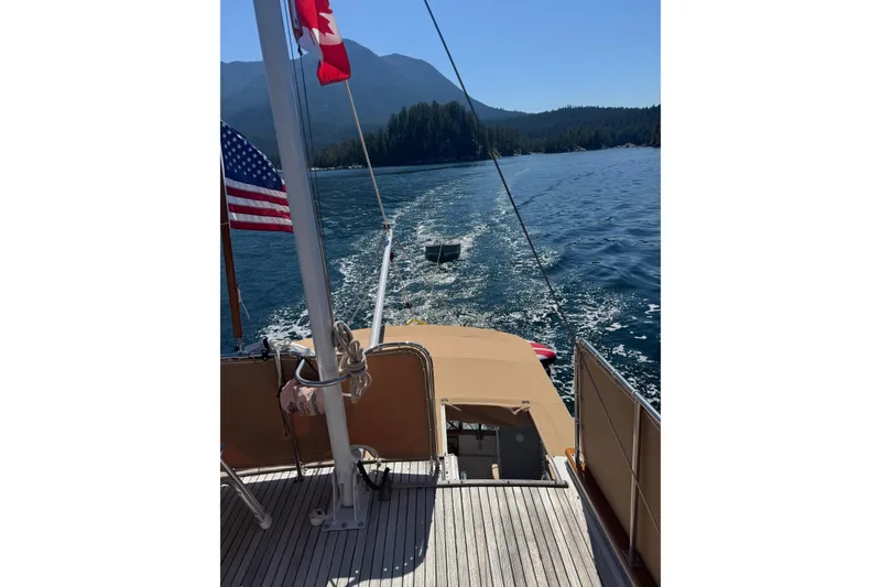 Slide: The Image of 1983 Grand Banks 32 Sedan cruising on a scenic lake with flags and mountainous backdrop. - 71